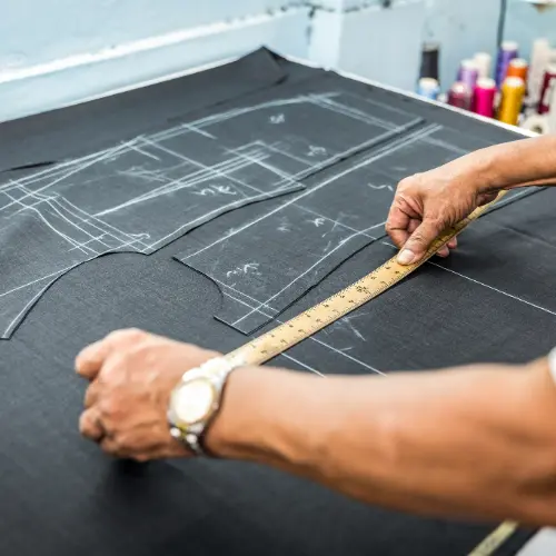 Tailor marking and cutting dark fabric to create a custom fitted suit at Vinny’s Custom Clothes Los Angeles